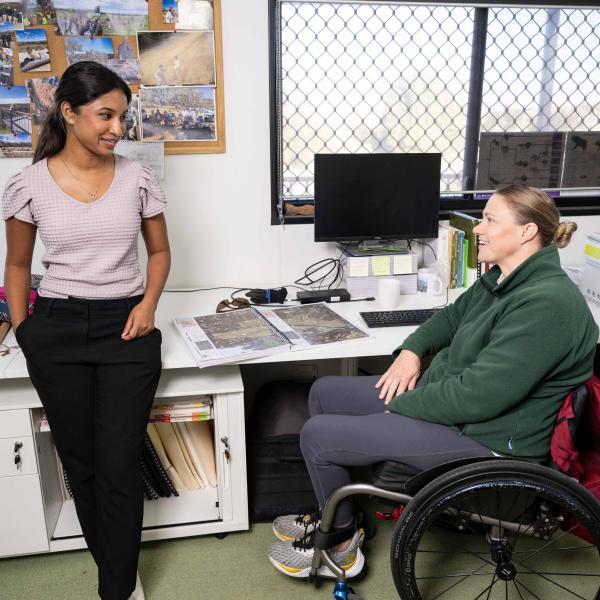 Two people in an office setting discussing something. One person is in a wheelchair.